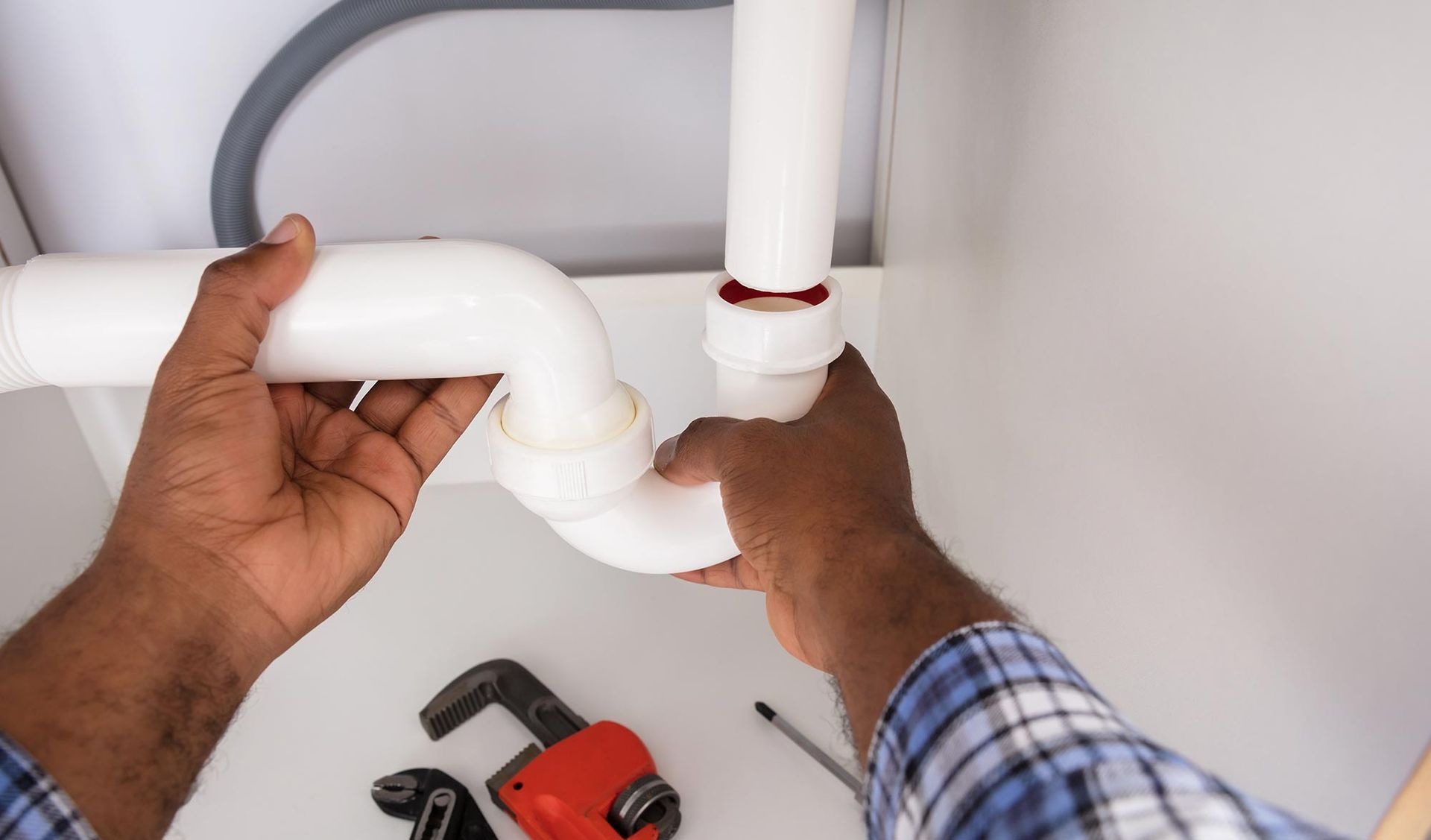 Hands fitting a white drain trap under a sink during a repair